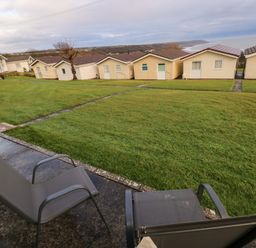 Two outdoor chairs on a patio facing a lawn with pathways and small houses beyond at Chalet 22 in Port Eynon