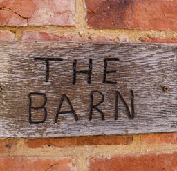A wooden sign with the words THE BARN on a brick wall at Home Farm Barn in Todenham near Moreton-In-Marsh