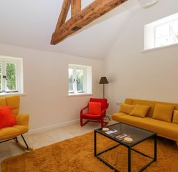 A living room with a yellow sofa yellow chair with orange cushions and a red chair around a glass coffee table at Home Farm Barn in Todenham near Moreton-In-Marsh