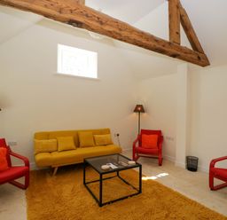 A living room with a yellow sofa red armchairs a black glass coffee table and wooden beams at Home Farm Barn Todenham near Moreton-In-Marsh