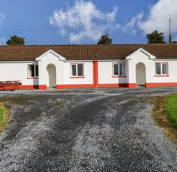 A bungalow with white walls and red trims on a gravel driveway with green grass on either side at Robins Roost 2 in Cornamona County Galway