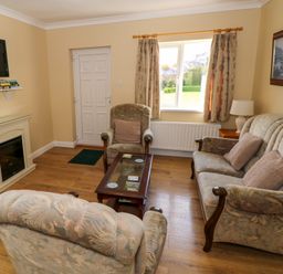 A living room with a sofa and two armchairs a coffee table a fireplace a wall-mounted TV and a window at Robin's Roost 2 in Cornamona County Galway
