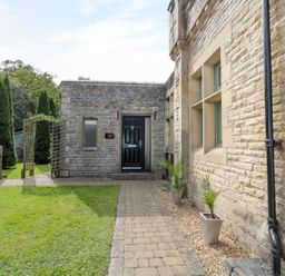 A stone building entrance with a black door potted plants along a brick pathway and tall trees in the background at Walworth Castle Lodge in Walworth near Darlington
