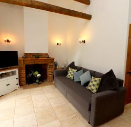A living room with a gray sofa with pillows a television on a white cabinet and a brick fireplace at Christon Well Cottage Christon Bank near Embleton