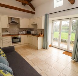 A kitchen living area with cream cabinets tiled floor and glass doors opening to a garden at Christon Well Cottage Christon Bank near Embleton