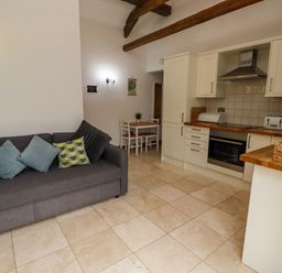 A kitchen with white cabinets a gray sofa with patterned cushions and a small dining table with chairs at Christon Well Cottage in Christon Bank near Embleton