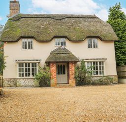 A thatched roof cottage with brick porch and multiple windows surrounded by trees at Moles Cottage in Farnham near Sixpenny Handley