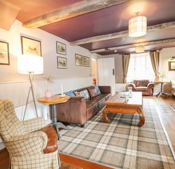 A living room with a brown leather sofa a plaid armchair wooden table and a fireplace at Moles Cottage Farnham near Sixpenny Handley