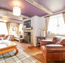 A living room with leather armchairs a wooden coffee table fireplace and a mounted television at Moles Cottage Farnham near Sixpenny Handley