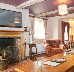 A living room with a fireplace a leather armchair a wooden coffee table and a mounted television at Moles Cottage in Farnham near Sixpenny Handley