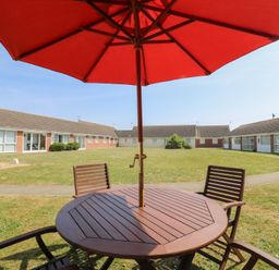 An outdoor wooden table with chairs and a red umbrella in a grassy courtyard surrounded by single-story buildings at 1 Kessingland Cottages in Kessingland