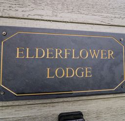A sign with the text Elderflower Lodge mounted on a wooden wall at Elderflower Lodge in Allithwaite near Cartmel