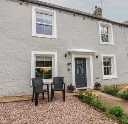 A house with a door and two chairs in front at 1 Brookside in Warcop