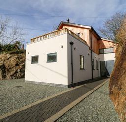 A modern two story house with a pathway and gravel ground between rocks at Ty Chwarel in Menai Bridge