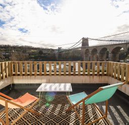 A balcony with two lounge chairs and a table overlooking a bridge and river at Ty Chwarel in Menai Bridge