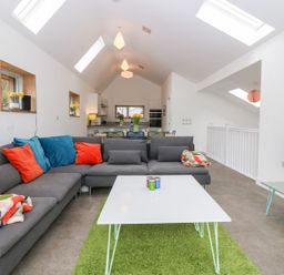 A living room with a gray sectional sofa and colorful cushions near a white coffee table on a green rug at Ty Chwarel in Menai Bridge