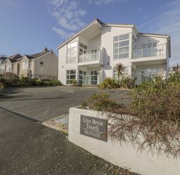 A two-story white house with balconies and large windows with a driveway and garden at Seaview in Benllech near Red Wharf Bay