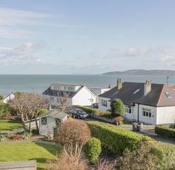 A garden with green bushes and a wooden shed near houses by the sea at Seaview in Benllech near Red Wharf Bay