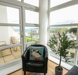 A sunroom with a black chair and green plant at Seaview in Benllech near Red Wharf Bay