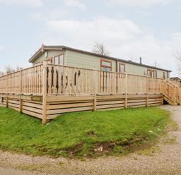 An exterior view of a mobile home with wooden railing and stairs in a grassy area at 6 Sherwood in Carnforth near Tewitfield