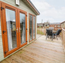 A wooden deck with a glass door and outdoor table and chairs at 6 Sherwood in Carnforth near Tewitfield