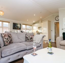 A living room with sofas a white table with a wine bottle and glass and a kitchen in the background at Finnbars Lodge in Richmond