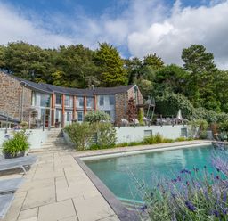 An outdoor swimming pool with lounge chairs and a stone house surrounded by trees at Curlew House in Cosheston