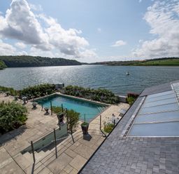 A patio with a swimming pool overlooking a river with green hills and a boat in the distance at Curlew House in Cosheston