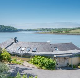A curved roof house by a river with green hills in the background at Curlew House in Cosheston