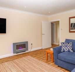 A living room with a blue sofa and patterned cushions a wooden side table and a mounted flat screen TV at West View in Northlew near Hatherleigh