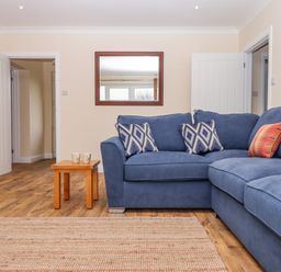 A living room with a blue corner sofa with cushions a wooden side table with two mugs a wall mirror and wooden flooring at West View in Northlew near Hatherleigh