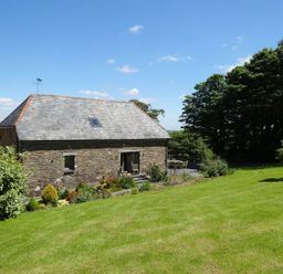 A stone house with a slate roof and a garden with bushes and a lawn at Swallows Reach in Halwell