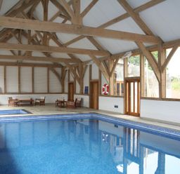 An indoor swimming pool with wooden beams and seating area at Swallows Reach in Halwell