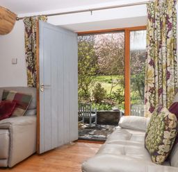 A living room with a door and window opening to a garden at Swallows Reach Halwell