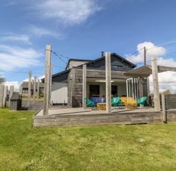 An outdoor wooden deck with chairs and pergola attached to a modern house with a grassy yard at Forest Lodge in Newborough