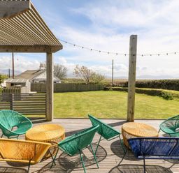 An outdoor patio with colorful chairs and tables overlooking a garden and a house in the distance at Forest Lodge in Newborough