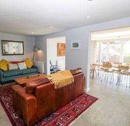 A living room with a brown leather sofa a teal fabric sofa a wooden coffee table and a dining area with chairs at Forest Lodge in Newborough
