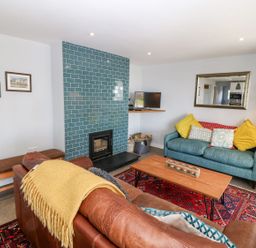 A living room with a brown leather sofa with a yellow throw a blue sofa with yellow and patterned cushions a wooden coffee table a red patterned rug a blue tiled fireplace a small TV on a corner shelf and framed photos on a white wall at Forest Lodge in Newborough