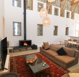 A living room with a fireplace two brown sofas a red rug and a dining area with a wooden table and chairs at Tithe Barn in Capel Mawr near Malltraeth