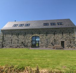 A stone barn with multiple windows and a large grass lawn at Tithe Barn in Capel Mawr near Malltraeth