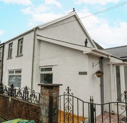 A white exterior house with an iron gate and brick wall a hanging flower basket and paved entrance at Meillion in Hirwaun