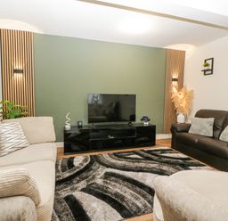 A living room with a beige sofa a brown sofa a black TV stand and a patterned rug at Meillion in Hirwaun