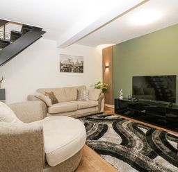 A living room with beige sofas a patterned rug a black television stand and a staircase at Meillion in Hirwaun
