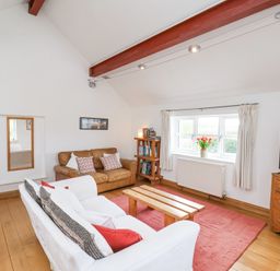 A living room with sofas, a wooden coffee table, a bookshelf, a TV on a wooden dresser, and a window with curtains at The Barn - Poplar Farm in Lower Dunsforth near Boroughbridge
