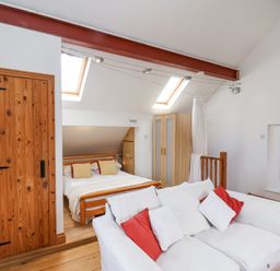 A bedroom with a wooden bed a white sofa with red and white cushions a wooden wardrobe and two skylight windows at The Barn - Poplar Farm in Lower Dunsforth near Boroughbridge