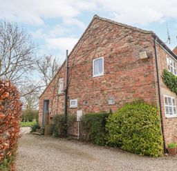 A brick house with small bushes and a gravel driveway at The Barn - Poplar Farm in Lower Dunsforth near Boroughbridge
