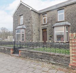 The exterior of a stone house with bay windows and a black wrought iron fence in front at Glan Yr Afon in Ystradgynlais