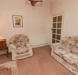 A living room with patterned armchair and sofa a wooden side table with lamp and a painting on the wall at Glan Yr Afon in Ystradgynlais