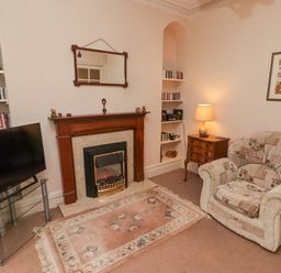 A living room with a fireplace a patterned armchair a lamp on a wooden side table and a television on a glass stand at Glan Yr Afon in Ystradgynlais