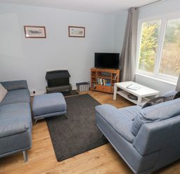 A living room with two blue sofas a small ottoman black rug TV on stand and large window at Kittiwake Apartment 22 Little Haven near Broad Haven
